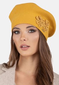 Béret en tricot jaune avec trois fleurs en feutre sur le côté, présentant une forme arrondie et une finition texturée.