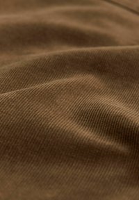 Brown corduroy fabric with vertical ribbed texture, showing folds and shadows, conveying a soft and tactile surface.