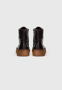 Bottes noires en cuir jusqu'à la cheville avec une finition texturée, des zips latéraux et une semelle marron contrastante ; dotées de détails tressés le long du bord.