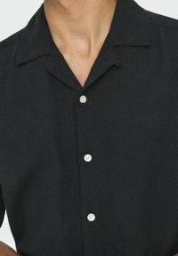 Camiseta negra de manga corta hecha de tela texturizada, con un cuello de solapa, cierre de cuatro botones y botones blancos.