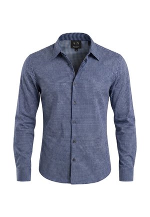 Camisa azul de manga larga con botones y un patrón geométrico blanco, con cuello abierto, mostrada sobre un fondo blanco liso.