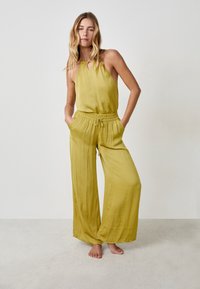 Mono amarillo sin mangas con cuello halter, cintura elástica y piernas anchas. Textura suave y diseño casual, con bolsillos laterales.