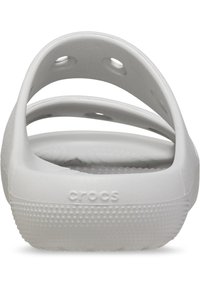 Ciabatte Crocs bianche con superficie testurizzata, design con schienale aperto, numerosi fori di ventilazione e il logo "CROCS" sul tallone.