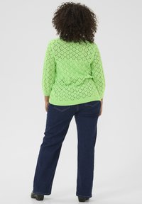 Sweter z dzianiny w diamentowy wzór w jaskrawym zielonym kolorze, z rękawami długości 3/4, zestawiony z ciemnoniebieskimi dżinsami, widok z tyłu.