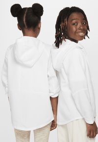 Chaqueta blanca con capucha y mangas largas, con una textura suave y un ajuste relajado. Dos niños mostrados de espaldas, con peinados naturales.