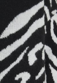 Der gestrickte Pullover hat ein schwarz-weiß gestreiftes Zebra-Muster, mit einer weichen Textur und dicken, warmen Fasern für zusätzlichen Komfort.