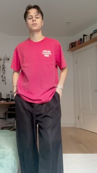 Camiseta de algodón fucsia con logo en el pecho, combinada con pantalones anchos negros, que tienen un ajuste relajado y una textura suave.