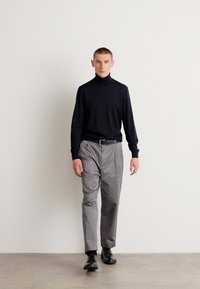 Fekete garbó pulóver, szürke szabott nadrág és fekete cipő. Slim fit, sima textúra és minimalista dizájn. Egyszínű, minta nélkül.