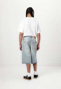 Lyseblå denimshorts med lige snit, baglomme og et lædermærke i taljen, parret med en hvid t-shirt og sorte sneakers.