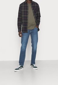 Plaid flannel shirt in dark green, black, and burgundy, over an olive T-shirt, paired with light blue jeans and green sneakers.