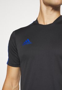 Camiseta deportiva negra con acentos azules en las mangas, hecha de una tela ligera y suave. Presenta un escote en pico y el logo de Adidas en el pecho.