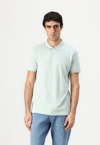 Lysegrønn polo skjorte med krage, to-knapp placket og brodert logo. Båret med lyseblå jeans. Glatt tekstur.
