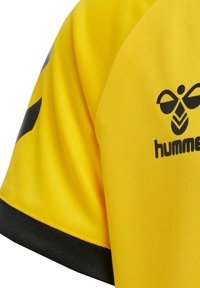 Gul sportströja med korta ärmar, svart kant i nederkant och en svart logotyp med en stiliserad bi och texten "hummel".