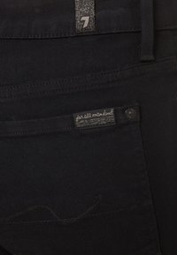 Pantalones de mezclilla negros con etiqueta de tela "for all mankind" en el bolsillo trasero y detalle de remache de marca.