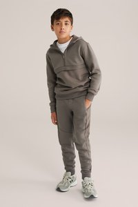Grå tvådelad sportoutfit bestående av en zip-up hoodie med texturerade paneler och matchande tapered byxor. Bärs med grå sneakers.