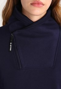 Marinblå sweatshirt med hög krage, utrustad med en sned dragkedja och G-Star-logotyp. Mjukt, tjockt tyg med en slät textur.