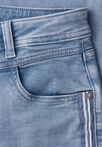 Nærbillede af lyseblå denimjeanslomme med stribet stofdetalje og synlig syning på linningen og bæltestrop.