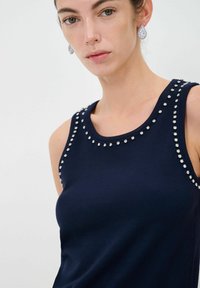 Top senza maniche di colore blu navy realizzato in tessuto liscio, caratterizzato da borchie argentate lungo il collo stondato, che mette in risalto il design semplice ma decorativo.