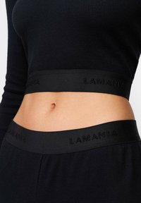 Fekete bordázott crop top sima derékpánttal, kiemelkedő "LAMANIA" logóval. Az anyag rugalmasnak és testhez simulónak tűnik.