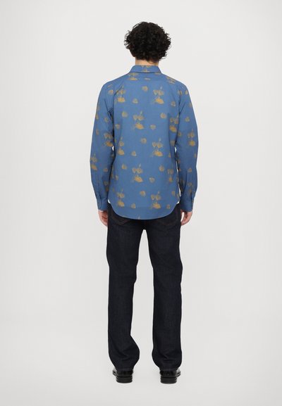 Camisa azul de manga larga con patrón de hojas doradas, cuello abotonado y diseño completo en la espalda. Combinada con pantalones de mezclilla oscuros y zapatos negros.