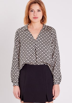 Blusa a maniche lunghe in crema con un motivo a rombi neri, dotata di colletto a V e leggero drappeggio, abbinata a una gonna nera aderente.