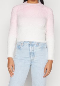 Sweter z miękkiego dzianego materiału z efektem ombre, przechodzącym od jasnoróżowego do białego. Długie rękawy, okrągły dekolt, zestawiony z jasnoniebieskimi dżinsami.