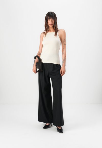 Crème geribbelde tanktop gecombineerd met zwarte wijde broek en zwarte hoge hakken, met een kleine zwarte tas. Soepele textuur, minimalistisch ontwerp.
