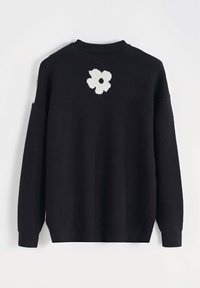 Pull en tricot noir avec un col rond, présentant un motif floral blanc au dos. Coupe décontractée avec des manches longues et des poignets côtelés.