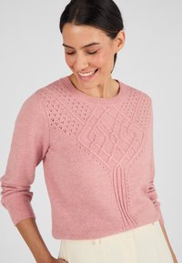 Lichtroze gebreide trui met textuurpatronen, een ronde halslijn en driekwartmouwen. Accentueert met oogjesdetails en een cropped pasvorm.