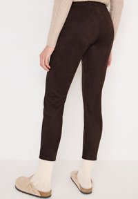 Brązowe legginsy z faux zamszu o dopasowanym kroju. Modelka nosi je z jasnymi, dzianinowymi skarpetkami i beżowymi butami wsuwanymi.
