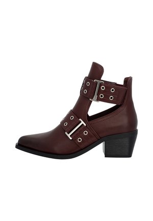 Braune Leder-Ankle-Boots mit spitzem Zehenbereich, doppelten Riemen mit Schnallen, ausgeschnittenem Design und schrägem schwarzen Absatz. Glatte Oberfläche mit dekorativen Hardware-Akzenten.