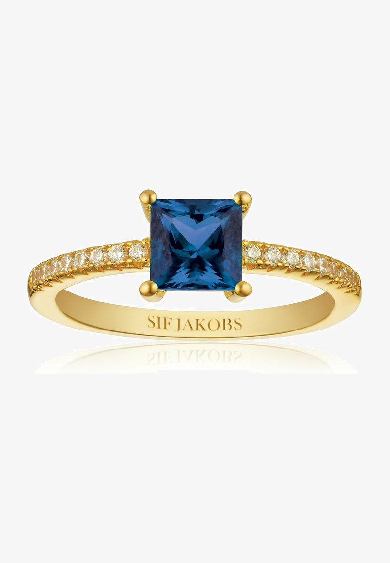 Guld ring med en stor firkantet blå sten i midten, prydet med små klare sten langs båndet. Indgraveret branding synlig.