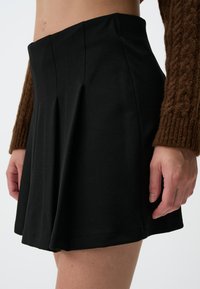 Zwarte geplooide rok van zacht materiaal, met een aansluitende tailleband en een uitlopende silhouet, die een gladde textuur en een keurige zoom heeft.