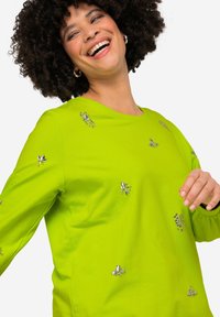 Camisa de manga larga de un brillante color verde lima, con adornos decorativos de rhinestone en forma de flores en el frente y las mangas.