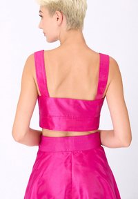 Crop top en satin fuchsia avec de larges bretelles et un dos droit, affichant une coupe ajustée et une texture lisse. Sans embellissements notables.