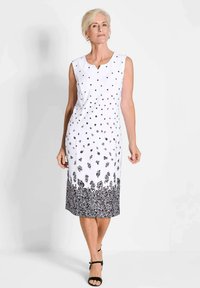Weißes ärmelloses Kleid mit schwarzen Blumenmustern und einem spitzenartigen Saum. Hat einen leichten V-Ausschnitt und eine figurbetonte Silhouette, strukturiertes Gewebe.