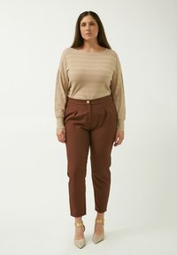 Maglione beige a coste con maniche lunghe, abbinato a pantaloni marroni svasati con pieghe frontali e un bottone dorato. Scarpe con tacco argentate.