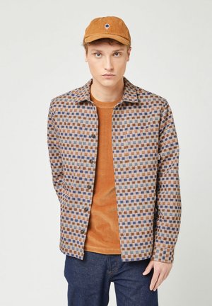 Geruite overhemd met knopen in bruine, blauwe en grijze tinten; oranje corduroy crewneck eronder. Bijpassende oranje pet met boomlogo.