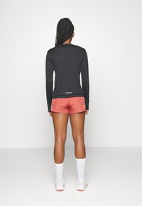Svart långärmad tröja med rund halsringning, kombinerad med rosa shorts. Vita strumpklädda fötter syns, vilket fulländar den atletiska outfiten.