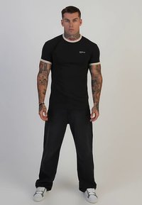 Maglietta nera con scollo e maniche a costine bianche a contrasto, abbinata a jeans scuri larghi e sneakers bianche.