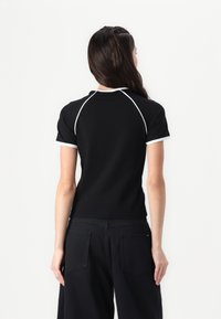 Svart kortärmad polo t-shirt med vit kant runt kragen och ärmarna, med en figurnära design och en mjuk bomullstextur.
