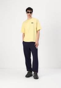 Yellow cotton t-shirt with a small green logo, paired with navy sweatpants featuring a white graphic, and black sneakers.