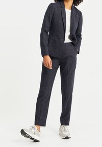 Marinblå texturerad tvådelad kostym med en figursydd kavaj och skräddarsydda byxor, i kombination med ljusgrå sneakers. Enkel vit t-shirt under.