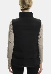 Sort puffervest med høj krave, der har en glat tekstur og en tætsiddende pasform. Bagsiden har en vandret søm og let puffet effekt.