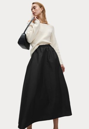 Schwarzer Maxirock mit elastischem Bund, kombiniert mit einem cremefarbenen Pullover. Der Stoff ist glatt und hat eine leicht strukturierte Silhouette.