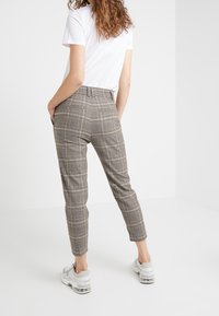 Beżowe spodnie w kratę o dopasowanym kroju, z wysokim stanem, dwoma tylnymi kieszeniami i mankietami u dołu, zestawione z białym t-shirtem i trampkami.
