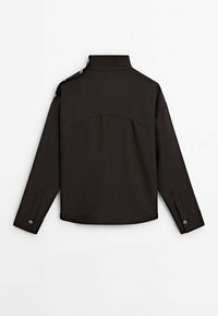 Giacca marrone scuro con colletto strutturato, dettagli con bottoni sulle spalle e maniche lunghe con polsini. Tessuto di texture liscia.