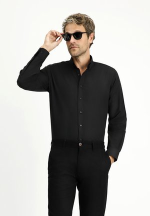 Camisa negra de manga larga con cierre de botones, tejido suave, diseño elegante, combinada con pantalones negros y gafas de sol. Look simple y moderno.