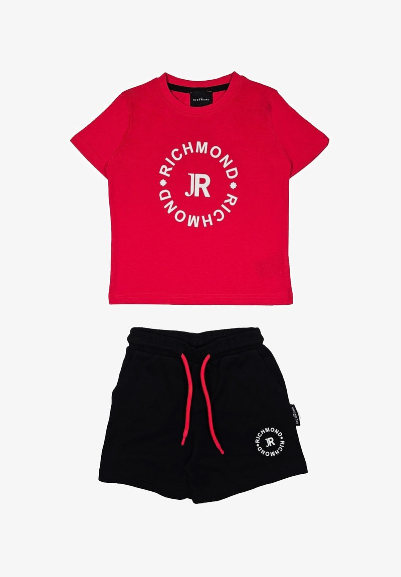 T-shirt in cotone rosso con testo grafico circolare bianco e logo; abbinato a pantaloni corti neri con elastico in vita e lacci rossi.