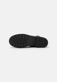 Semelle de chaussure en caoutchouc noir avec des rainures profondes et des indentations circulaires pour une meilleure adhérence. Plate et robuste avec une texture uniforme.